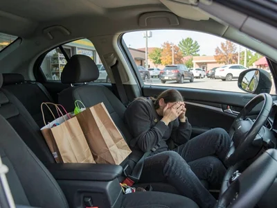 Woman crying in her parked car in a grocery store lot, shopping bags untouched i