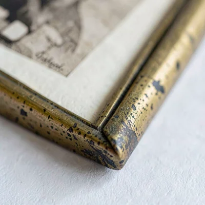 Mineral-cut close-up of a brass photo frame corner with patina, sepia print just