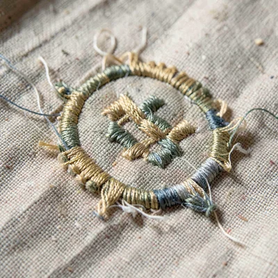 Worn-texture close-up of an embroidered monogram on linen, threads loosened and