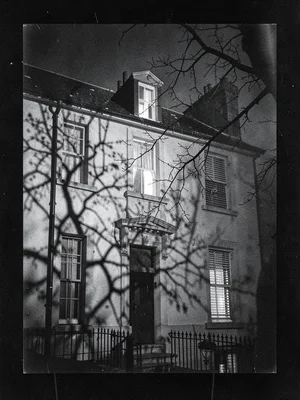 Georgian terrace at night, one lit window on the top floor, bare tree branches c