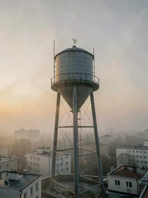 Pale dawn fog wraps a water tower's legs while its barrel emerges into clearer a