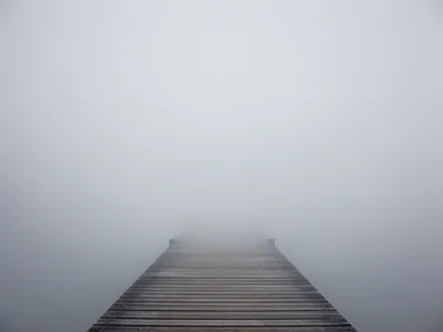 Foggy pier extending into nothingness, wooden planks vanishing into grey