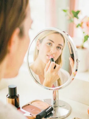 Woman applying lipstick using a compact mirror, only the mirror reflection sharp