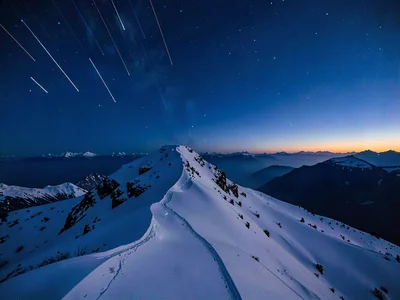 Star trails visible in deepening blue above a snow ridge at twilight