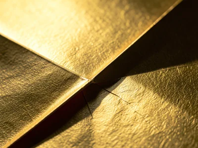 Reverse fold on gold foil paper, metallic surface crinkled at stress points, smo