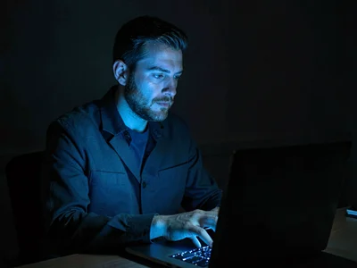 Person on video call in dark room, laptop screen the only light, professional fr