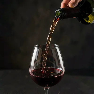 Macro lightbox study of a wine pour into a tumbler, dark seamless, raking key li