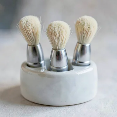 Mineral-cut macro of a porcelain brush rest holding three brushes, cool shadow v