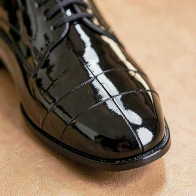 Mineral-cut detail of patent leather oxford toe with hairline cracks across the