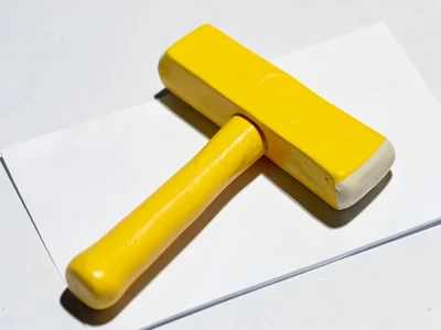 Blunt chunky clay hatchet in primary yellow with stubby cream-toned handle and o