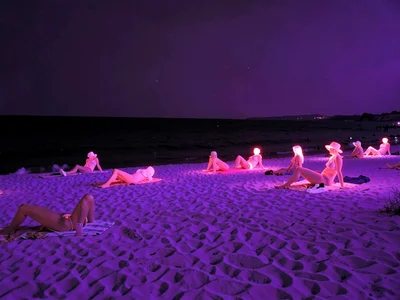 Beach scene in infrared where sand is purple and water is black and sunbathers g