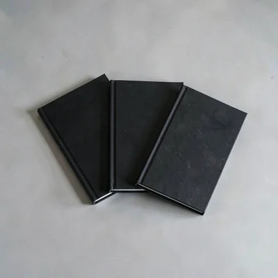 Minimal still of three identical black notebooks fanned on a pale ash desk, hair