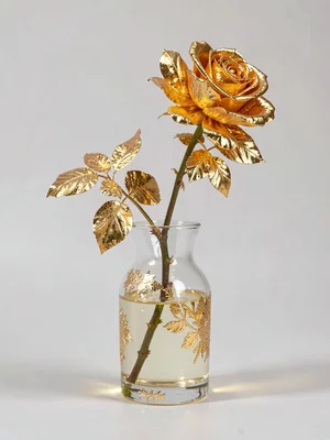A glass vase with water and a rose stem, the petals turned entirely to gold leaf