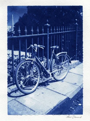 A bicycle locked to a wrought iron fence with its shadow on the sidewalk