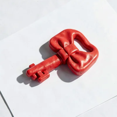 Oversized clay key with a primary-red bow and stubby teeth lying on plain white