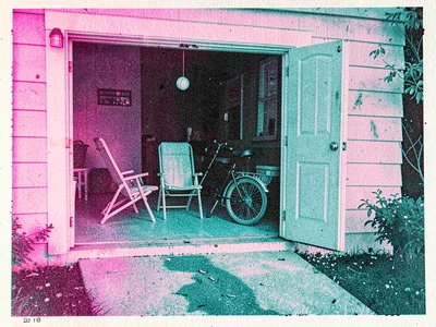The half-open garage door of a tract house revealing folded lawn chairs, a bicyc