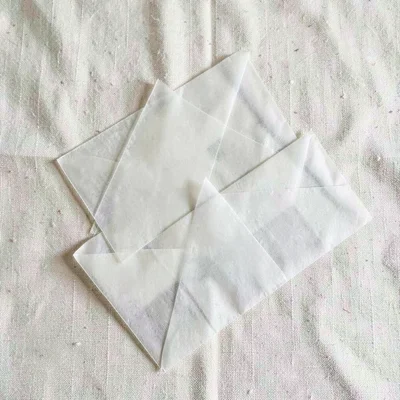 Top-down arrangement of three glassine envelopes stacked unevenly on cream linen