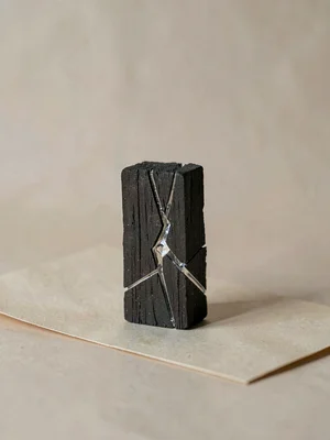 A solitary chunk of binchotan charcoal standing upright on beige paper, glassy f