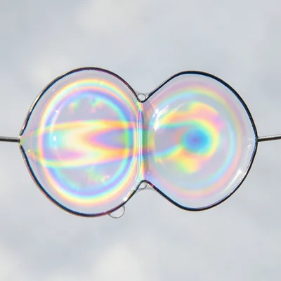 Two soap bubbles merging, the shared wall between them showing distinct interfer