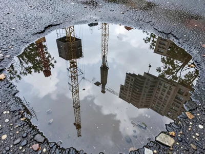 Construction site puddle reflecting crane and scaffolding, industrial skyline in