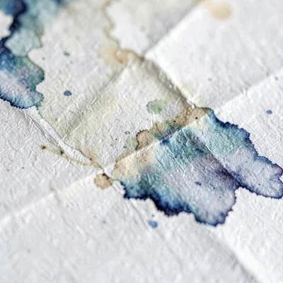 Macro of softly creased J-card paper with ink bleed, painterly fold shadows