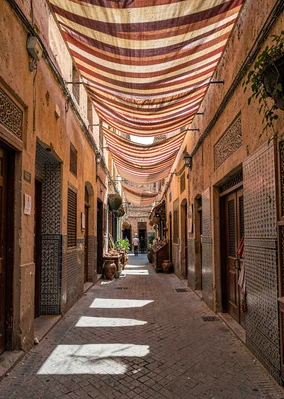 Geometric shadow play in Marrakech medina, narrow medina alley with striped fabr