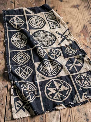 Worn Adinkra funeral cloth — aged symbols on dark ground, cloth draped and folde