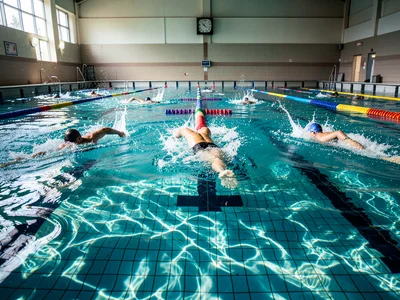 A swimming pool during adult lap swim — three lanes occupied, each swimmer at a 