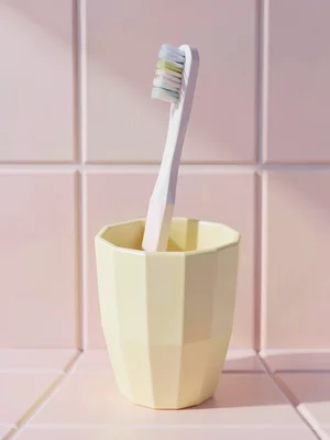 Solo faceted toothbrush standing in a butter-yellow cup against pastel pink tile