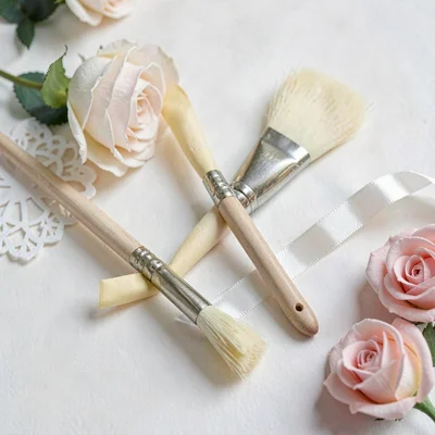 Papercraft still life of paper-cut brushes, ferrules and ribbon in butter and ro