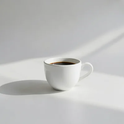 Minimalist photography of a single white coffee cup on a clean matte surface, soft natural window light, gentle shadow, 
