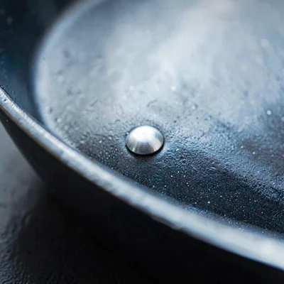 Tight mineral close-up of riveted handle joint on a saute pan, brushed steel riv