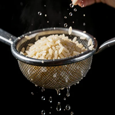 Macro-leaning composition of a steel sieve rinsing rice, droplets caught against