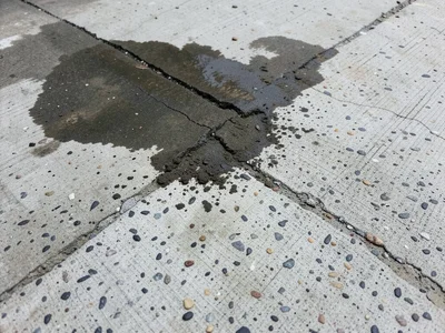 Concrete with dark water stain, wet patch spreading from corner creating two-ton