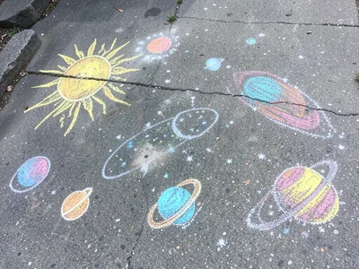 A chalk universe on a sidewalk: a sun, planets in order, each carefully colored,