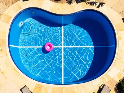 A kidney-shaped residential pool from above, the organic curve creating an asymm