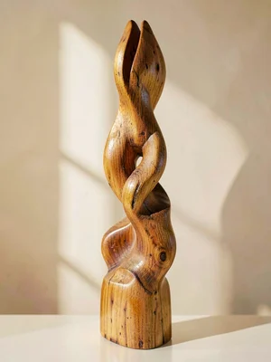 A tall carved wooden sculpture stands upright showing organic curving forms and