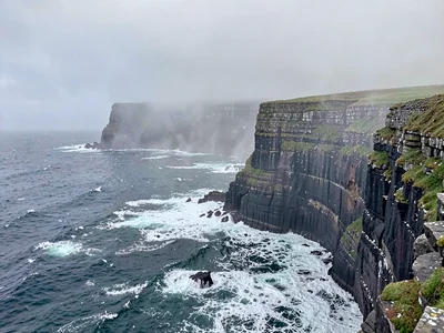 The Cliffs of Moher stretching into Atlantic mist, waves crashing white against 