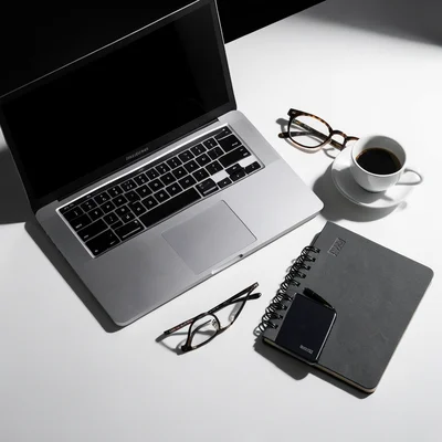 Desk essentials flat lay: laptop, phone, coffee, glasses, notebook on clean whit