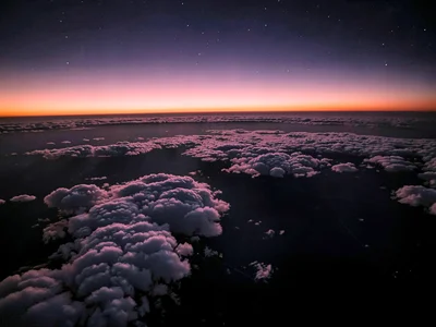 Thin clouds at high altitude catching sunrise pink against already-dark upper at