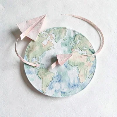 Layered papercraft of a paper airplane circling a stylized globe, blush and sage