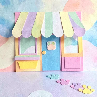 Playful cut-paper scene of a bakery awning with paw prints leading to the door, 