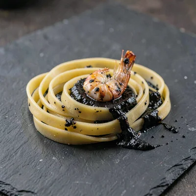 Single hand-pulled fresh-cut handmade pasta on dark slate with a smear of dark s