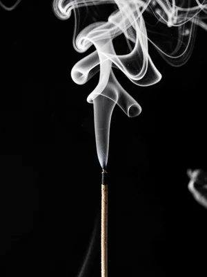 A lit incense stick, thin smoke column splitting into turbulent airflow above
