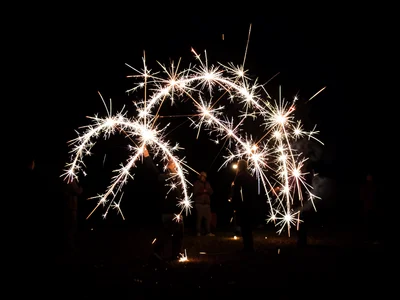 Multiple sparklers drawing shapes in dark, long exposure, figures barely visible