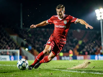 Soccer player striking the ball with perfect form, grass flying, evening floodli