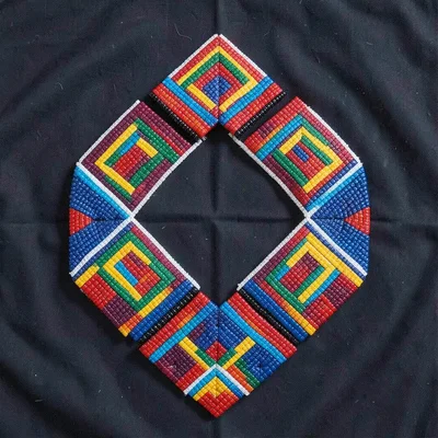 Traditional beaded neck ring (isigolwani) on dark fabric, studio flat-lay
