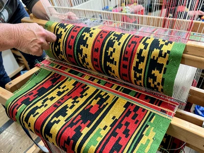 Traditional hand loom in use — shuttle mid-pass through colored warp threads