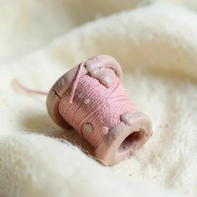Idle dusty-rose spool of thread with a slumped end and fingernail dents around i