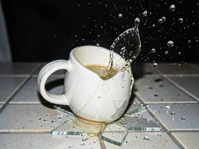 Ceramic mug shattering on tile with handle separating and liquid suspended